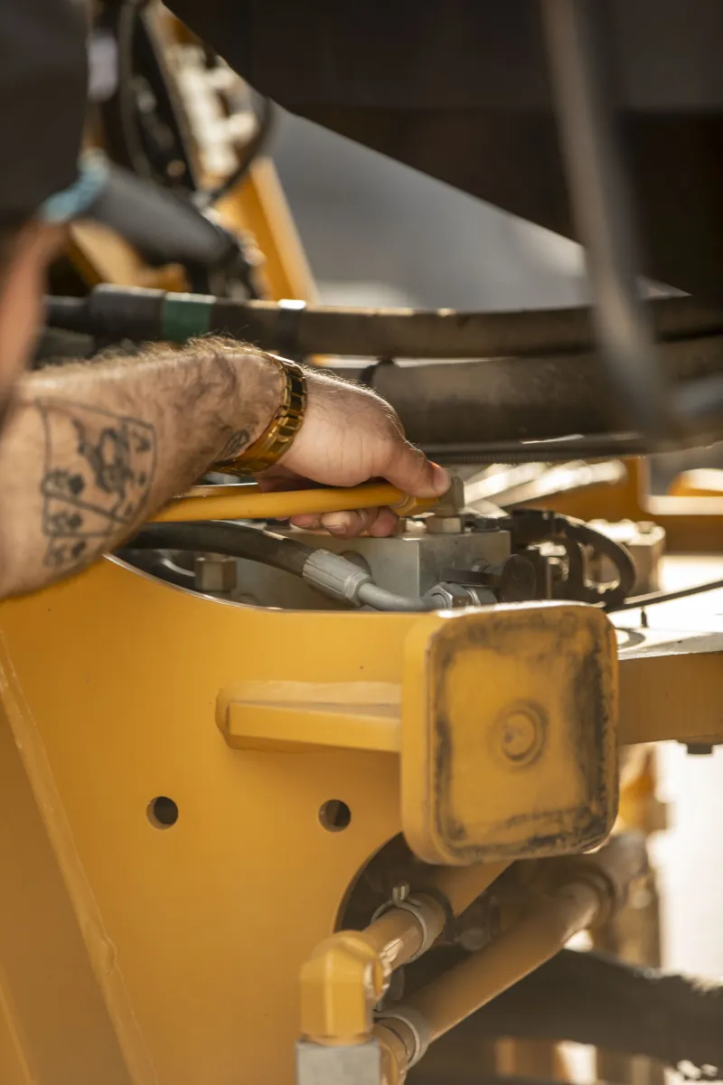 A tattooed arm reaching into a hydraulic linkage